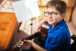 Portrait of a young boy with glasses practicing a song during a guitar lesson at home